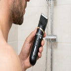 Person using a beard trimmer under running water in a bathroom.